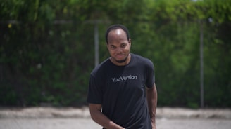 Side view of a model walking outdoors wearing a black t-shirt with a modern scripture print