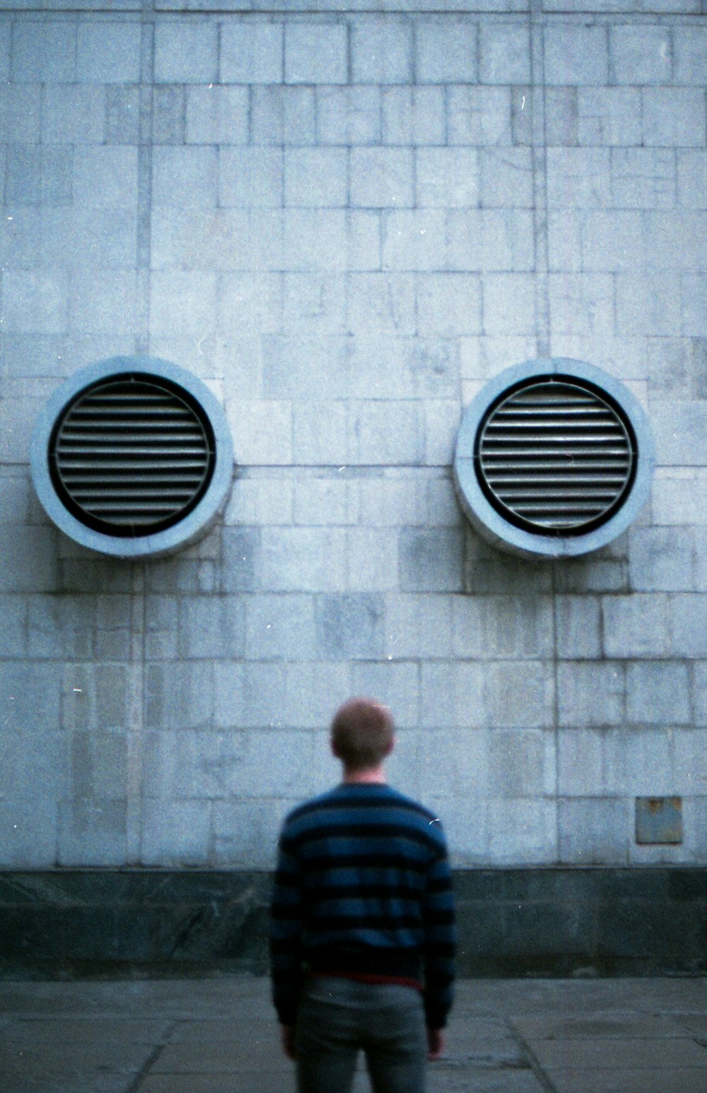 man in blue and black striped shirt standing in front of gray concrete wall