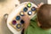 A child wearing a green shirt is sitting at a table, interacting with a tactile toy. The toy consists of a wooden board with several blue circular frames containing different textured materials like fabric and sandpaper. The child is focused on touching these textures.