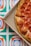 A pizza with pepperoni topping inside a pizza box. The background is a vivid, geometric pattern with green, blue, and orange shapes.