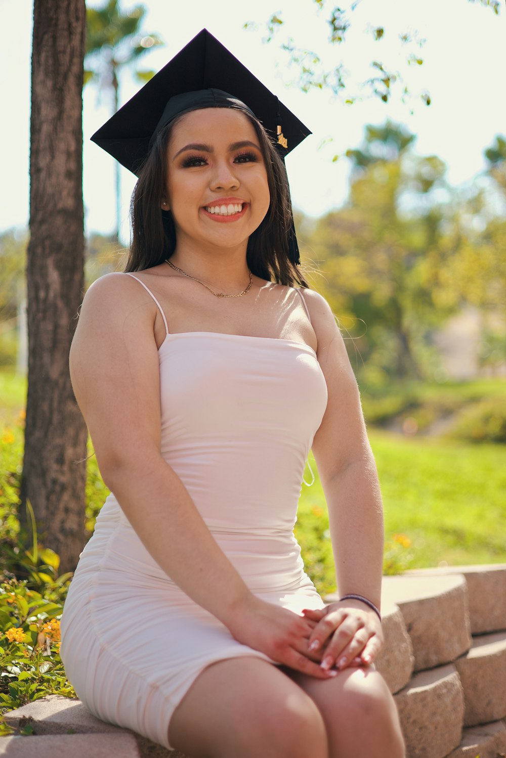 woman in white tank top and black academic hat sitting on brown wooden bench during daytime