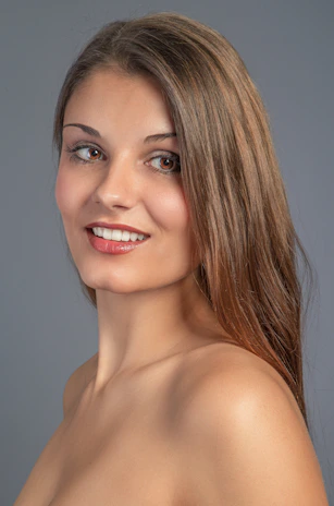 Smiling young woman with clear skin in a softly lit mint green background.