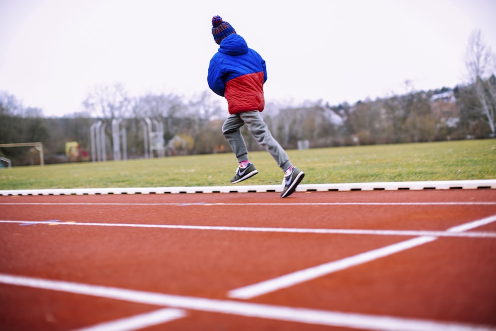 homme en veste bleue et pantalon gris courant sur le terrain d’athlétisme pendant la journée