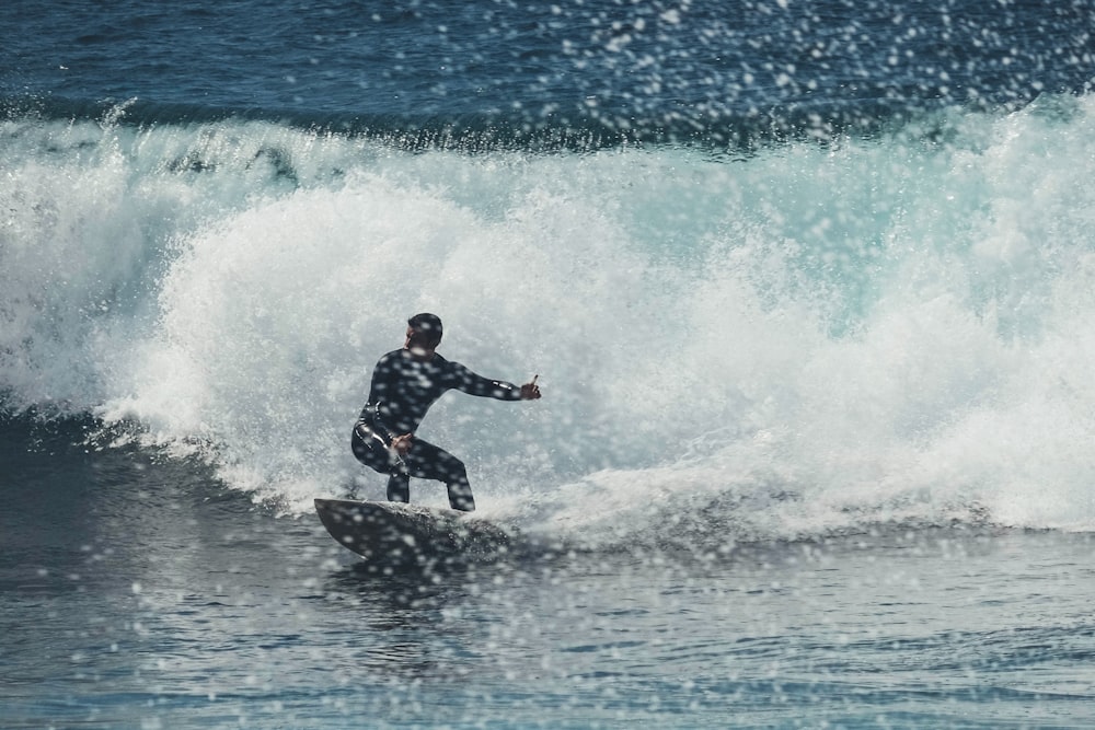 man in black wet suit surfing on sea waves during daytime