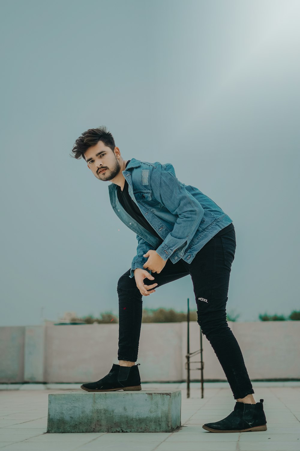 man in blue denim jacket and black pants standing on dock during daytime