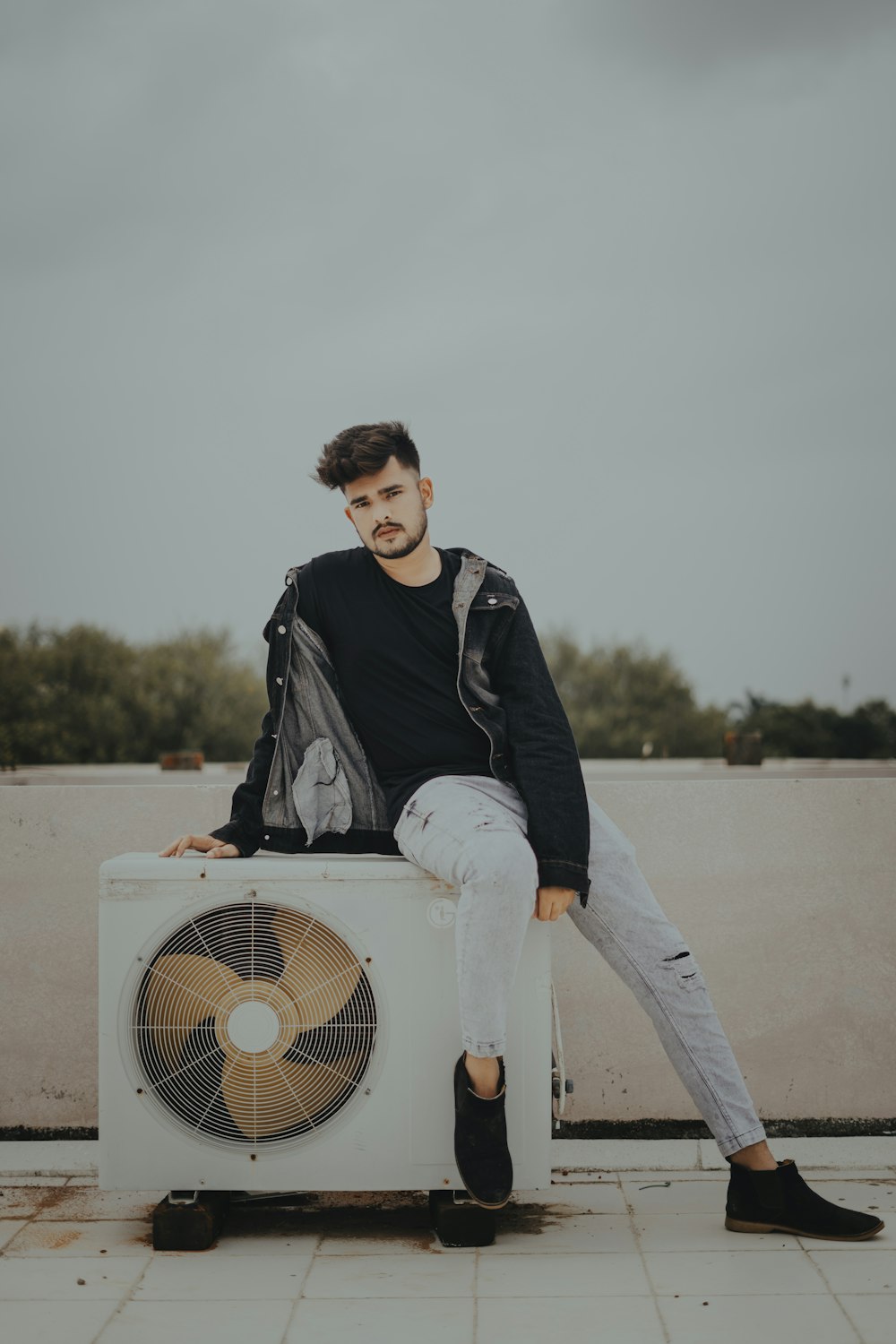 man in black jacket and white pants sitting on white box fan