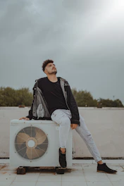 man in black jacket and white pants standing beside white box fan