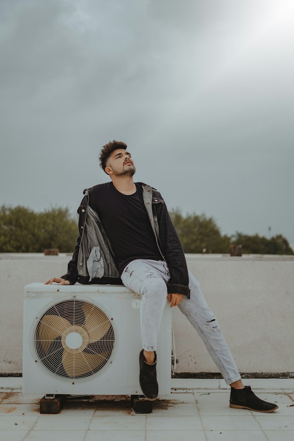 man in black jacket and white pants standing beside white box fan