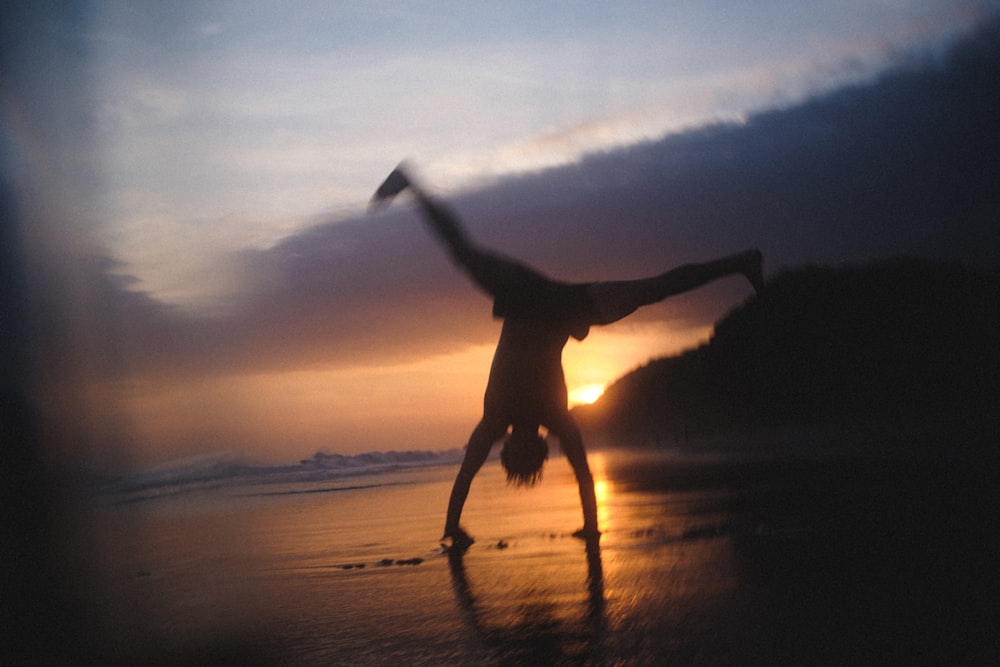 夕暮れ時に浜辺に飛び跳ねる女性のシルエット