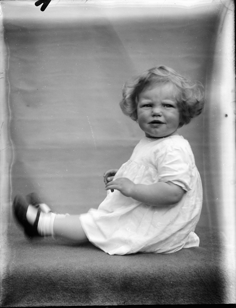 Photo en niveaux de gris d’une fille en robe blanche assise sur le sol