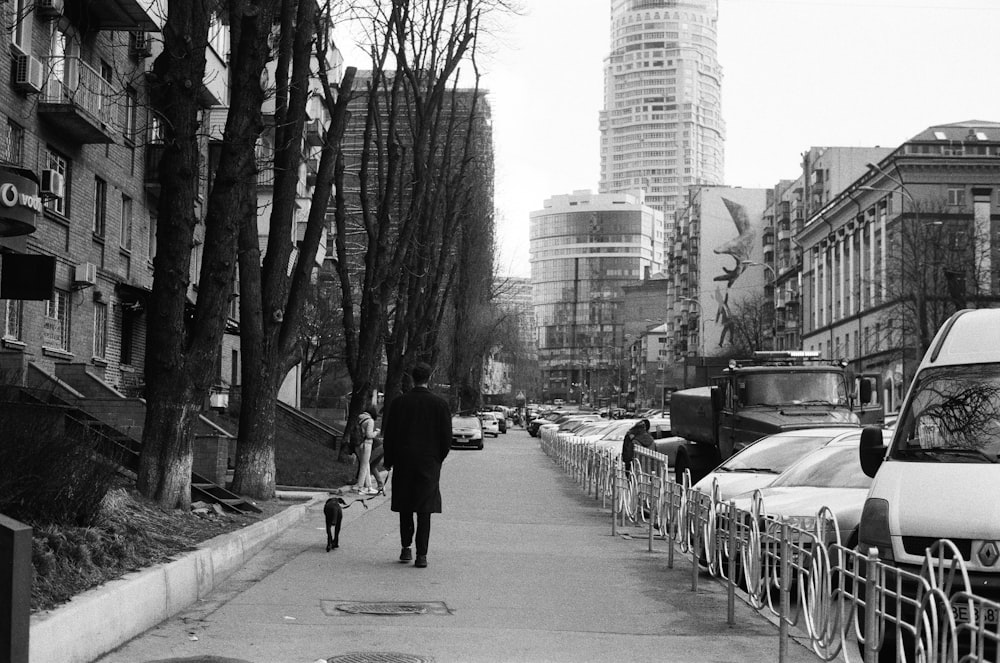 grayscale photo of man walking on sidewalk