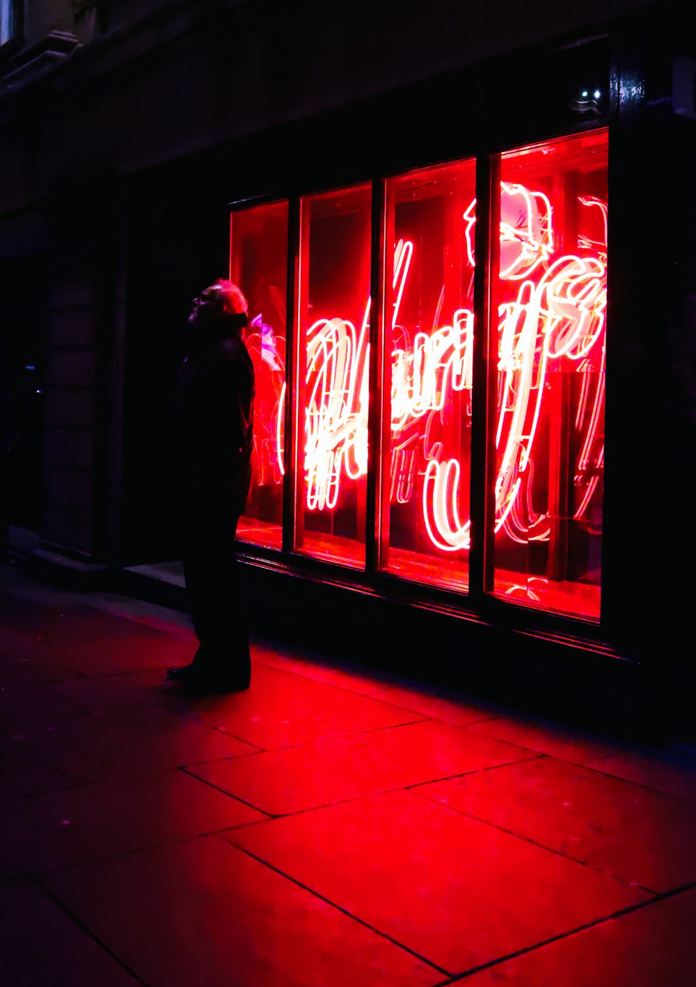 man in black jacket standing near red neon light signage