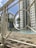 A swimming pool area surrounded by tall residential buildings. The pool is enclosed by a white metal fence, featuring geometric patterns. Palm trees add a tropical touch to the urban environment. The sky is clear with a few clouds.