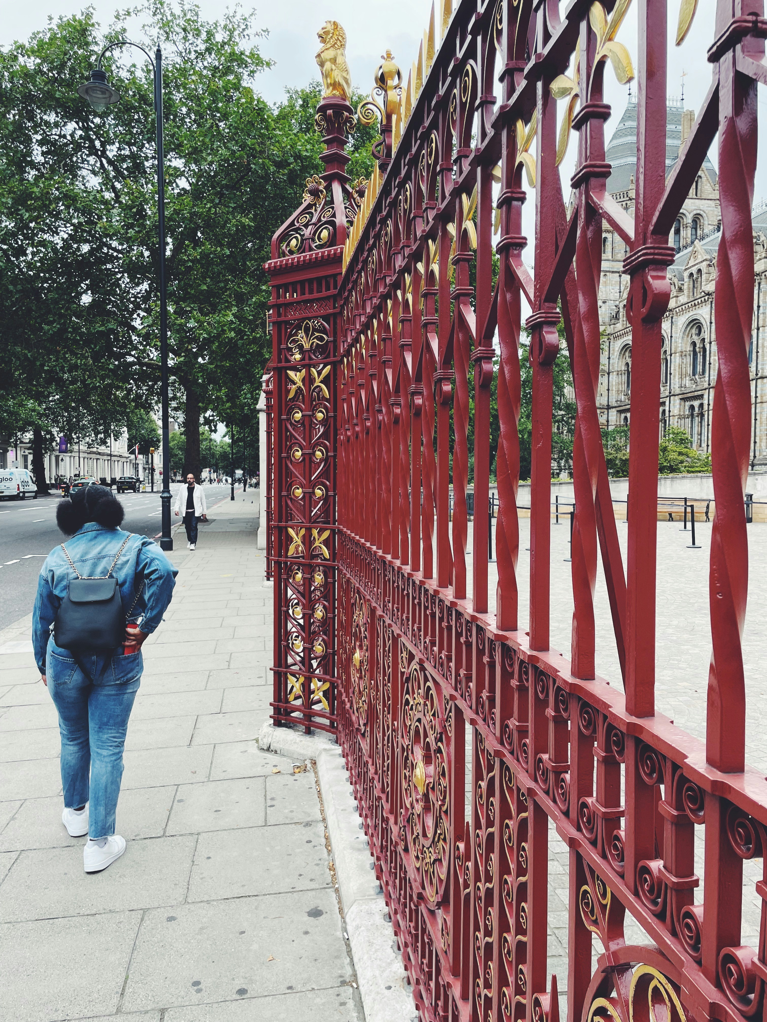 昼間、赤い金属の柵のそばに立つブルーデニムジーンズの男