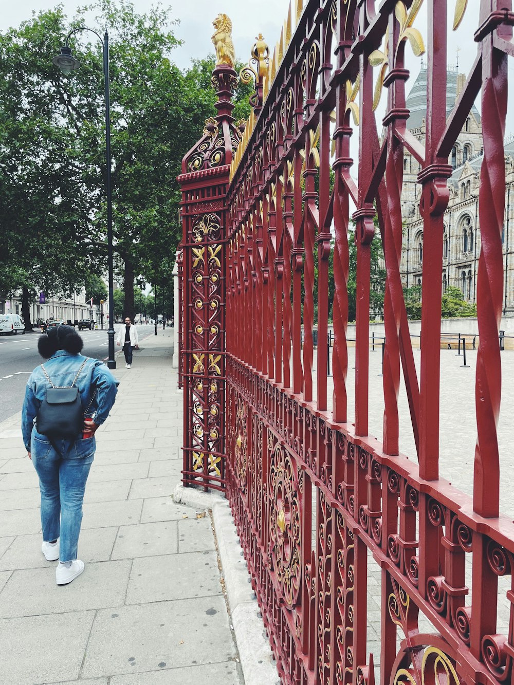 man in blue denim jeans standing near red metal fence during daytime