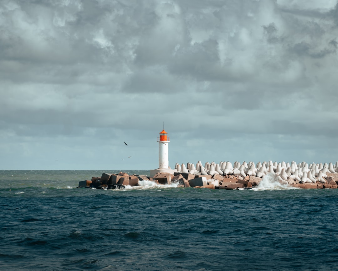 white lighthouse on the ocean under cloudy sky