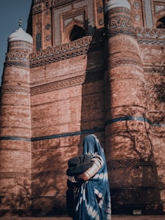 woman in gray hijab standing near brown brick wall