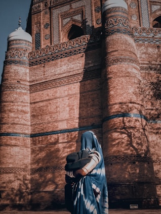 woman in gray hijab standing near brown brick wall
