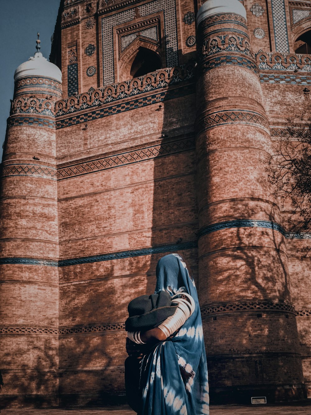 femme en hijab gris debout près d’un mur de briques brunes