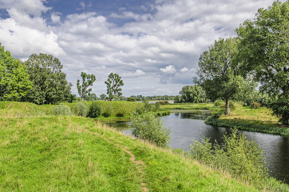 green grass field near river under cloudy sky during daytime