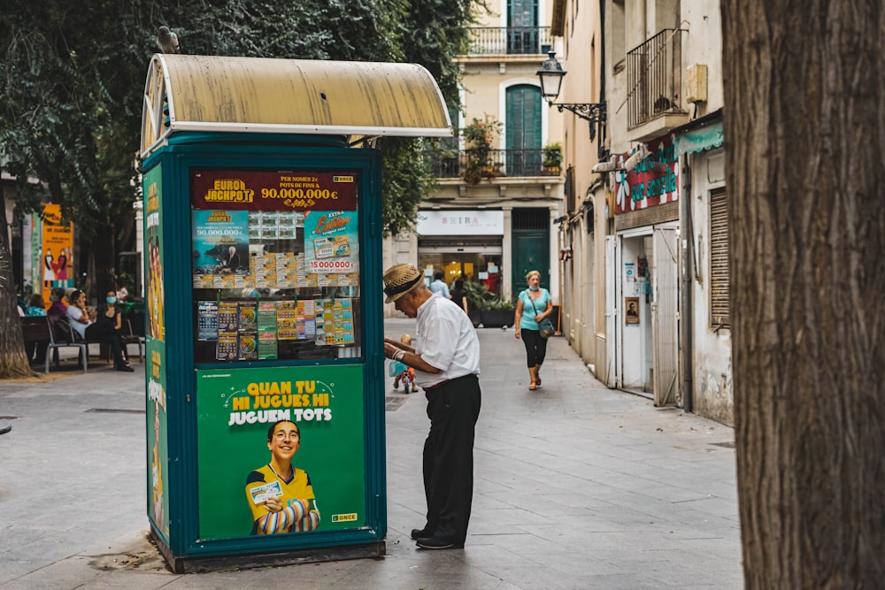 hombre con camisa de vestir blanca y pantalones negros de pie junto al puesto de comida azul y amarillo