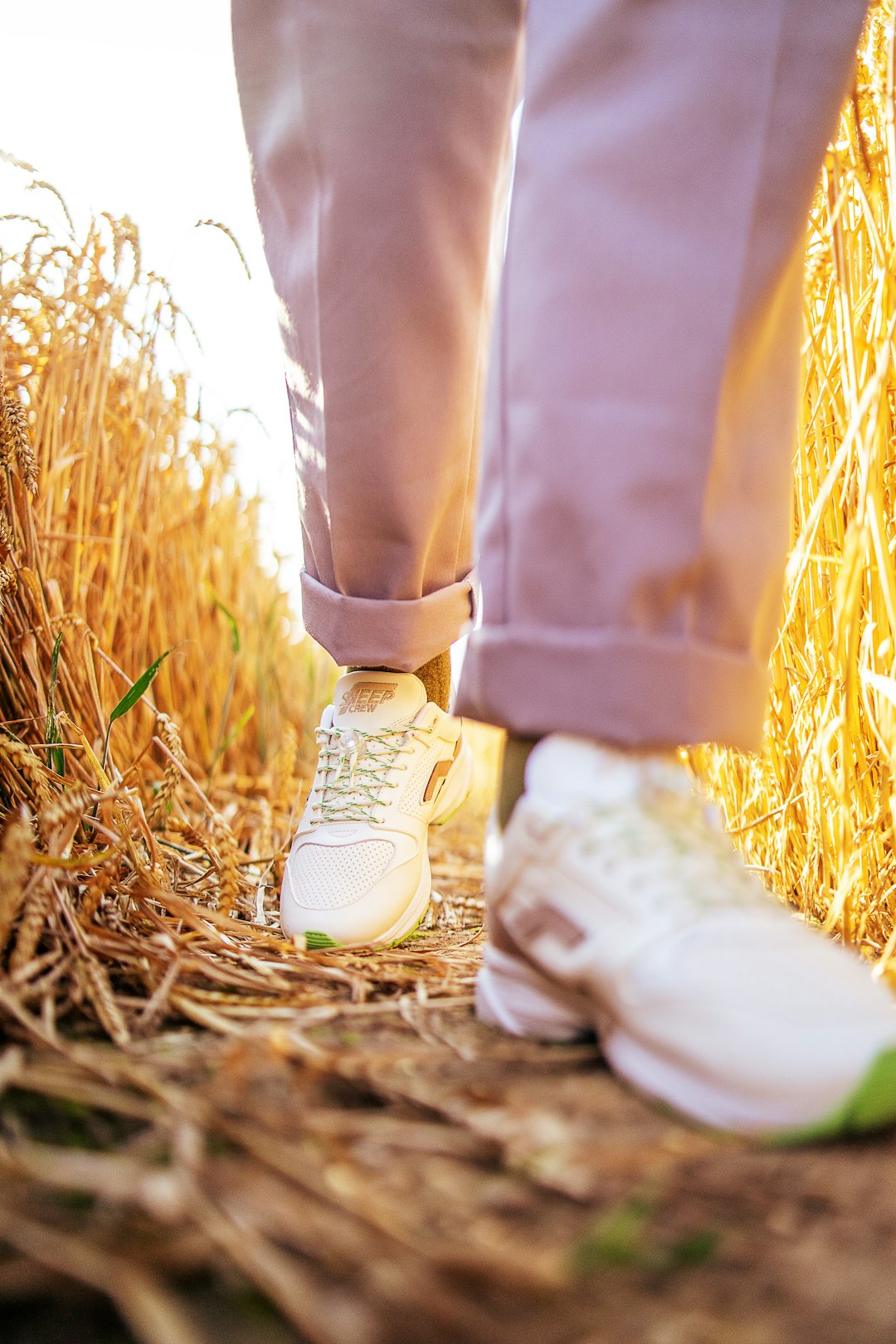 person in brown pants and white sneakers standing on brown grass field during daytime