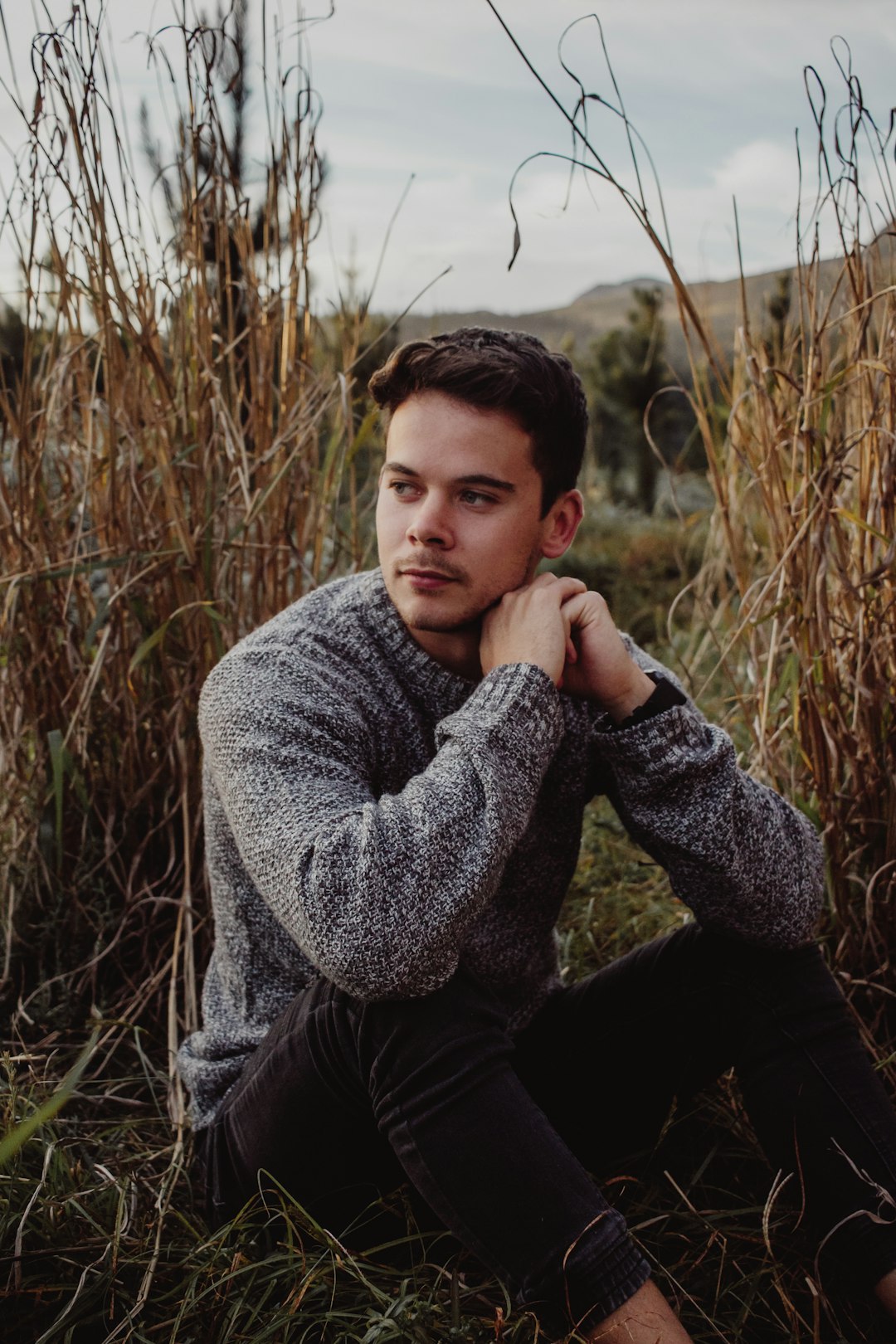 man in gray sweater sitting on grass field