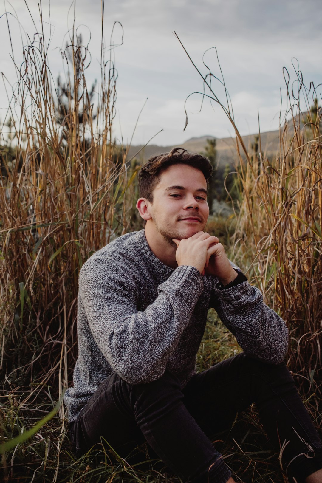 man in gray sweater sitting on brown grass field during daytime