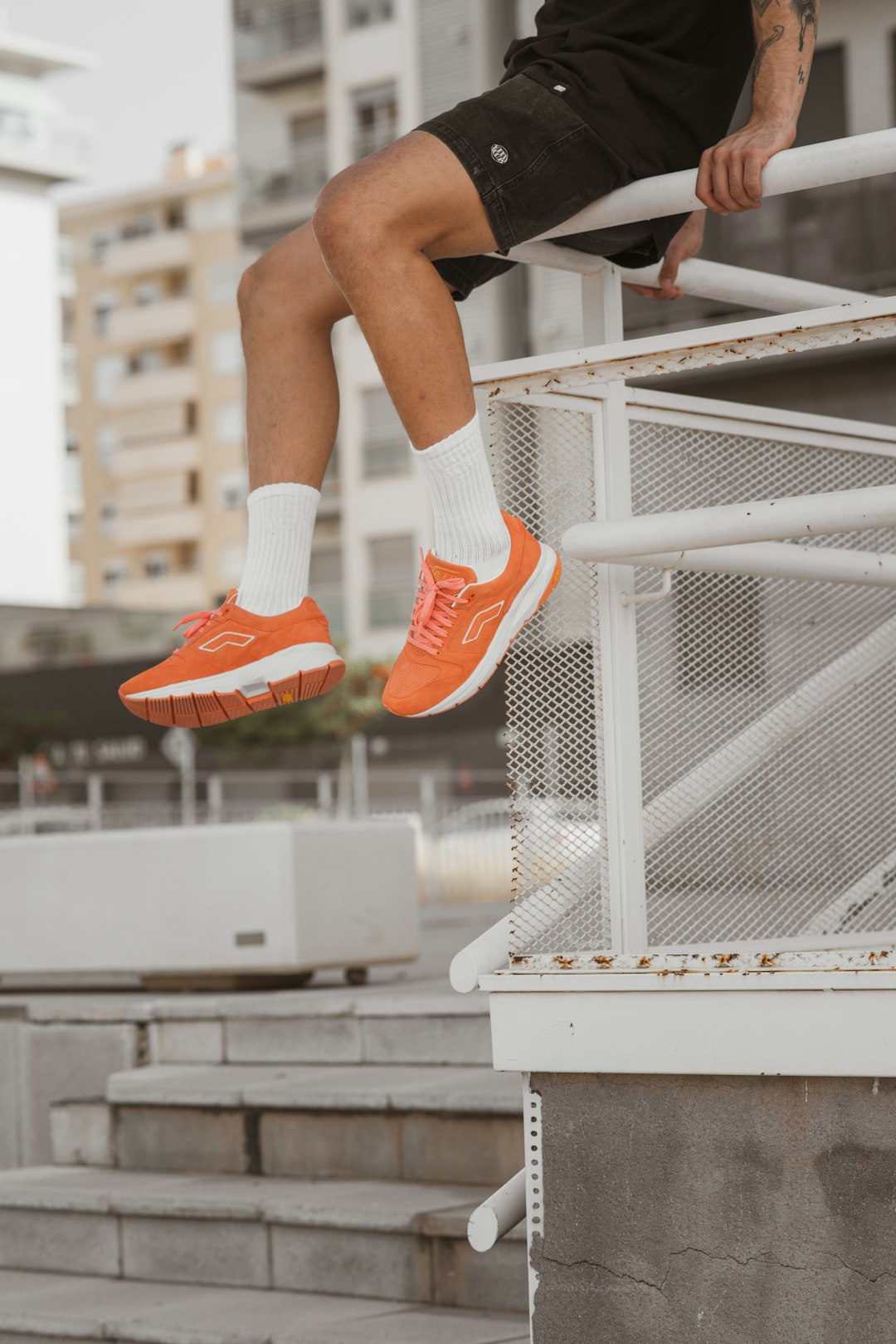 person in orange and white nike sneakers sitting on white metal railings