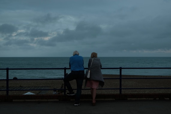 couple sitting on bench near sea during daytime