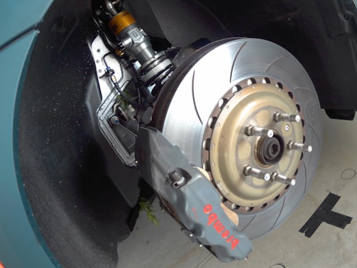 A close-up view of a car's braking system, featuring a large, ventilated brake disc with a high-performance brake caliper labeled 'Brembo'. The suspension components are visible, indicating advanced engineering. The metallic surfaces reflect light, suggesting new or well-maintained parts.