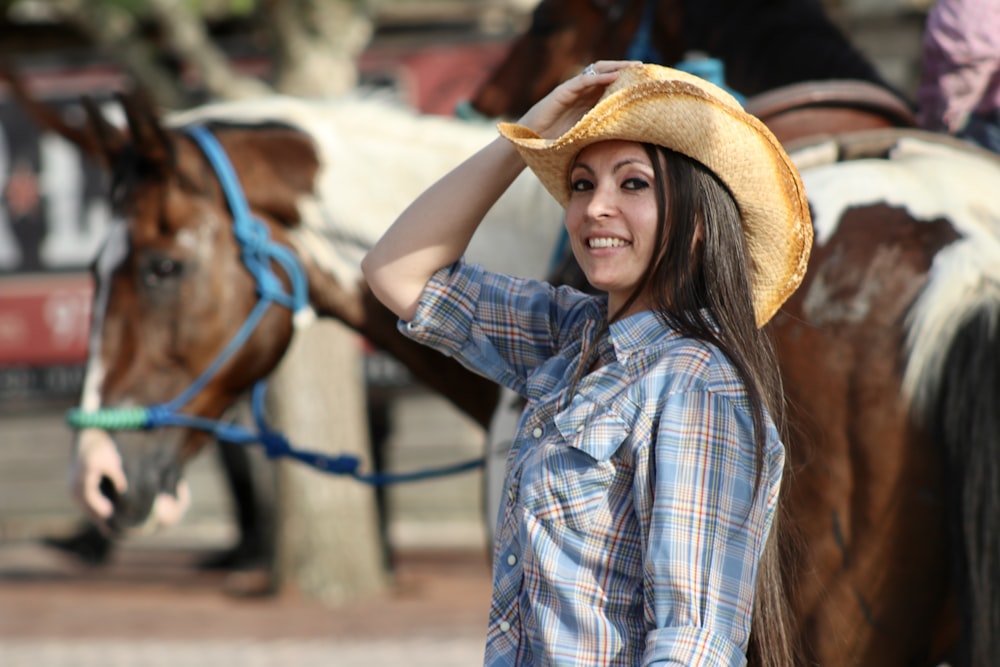 a woman wearing a cowboy hat standing next to horses