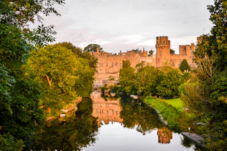 brown concrete castle near green trees and river during daytime