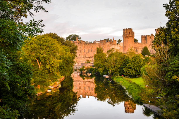 brown concrete castle near green trees and river during daytime