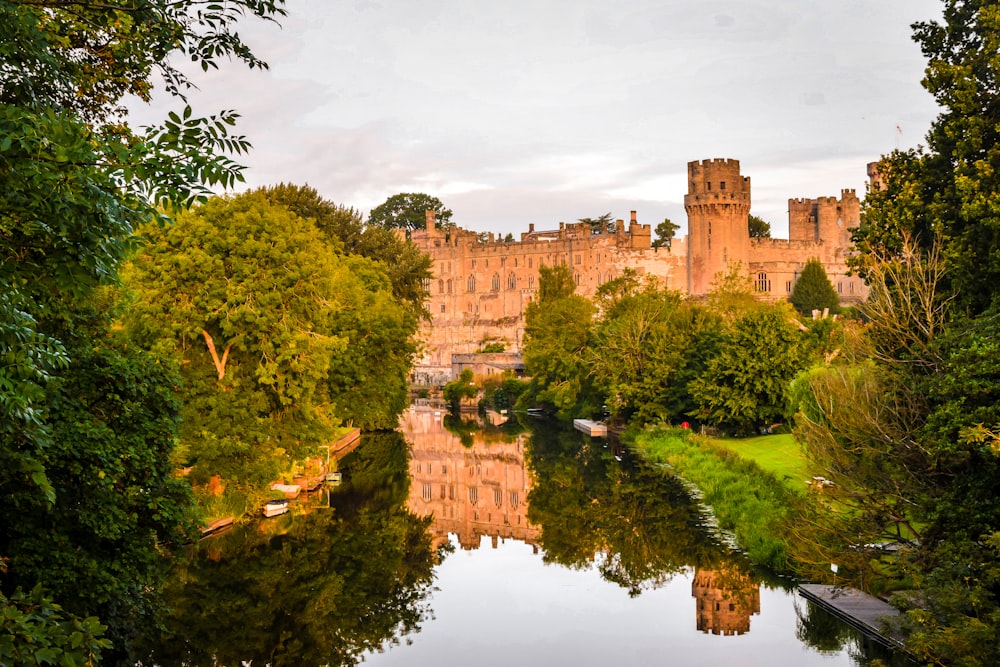 brown concrete castle near green trees and river during daytime