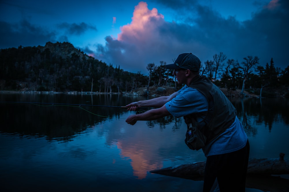 Hombre con sudadera con capucha azul de pie cerca del lago durante el día