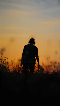 A silhouette walking alongside a shadow under a soft, glowing sky.