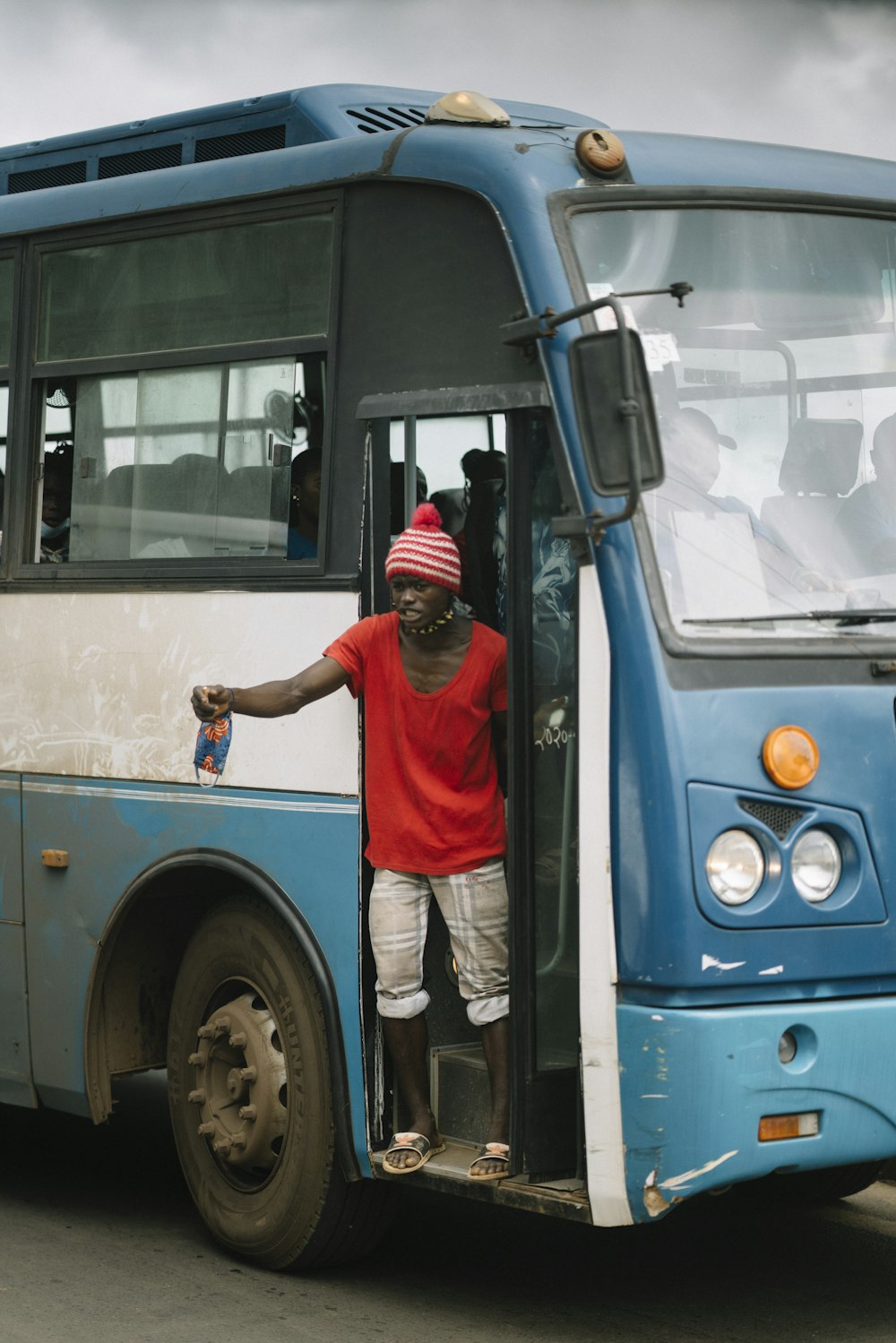 빨간 티셔츠와 흰 바지를 입은 남자가 낮에 파란 버스 앞에 서 있다