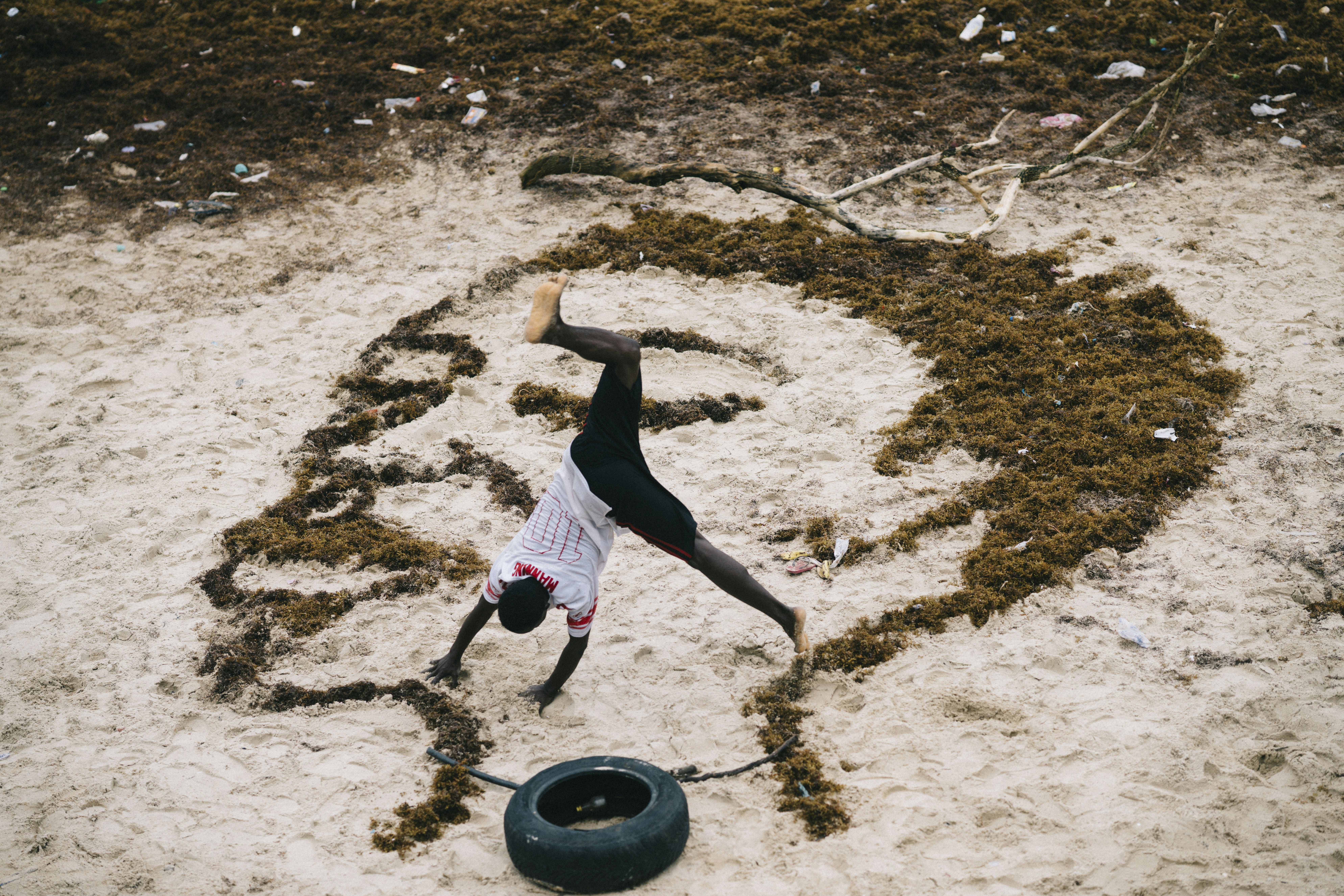 woman in black tank top and pink skirt standing on brown sand during daytime, Art work made out of seaweed