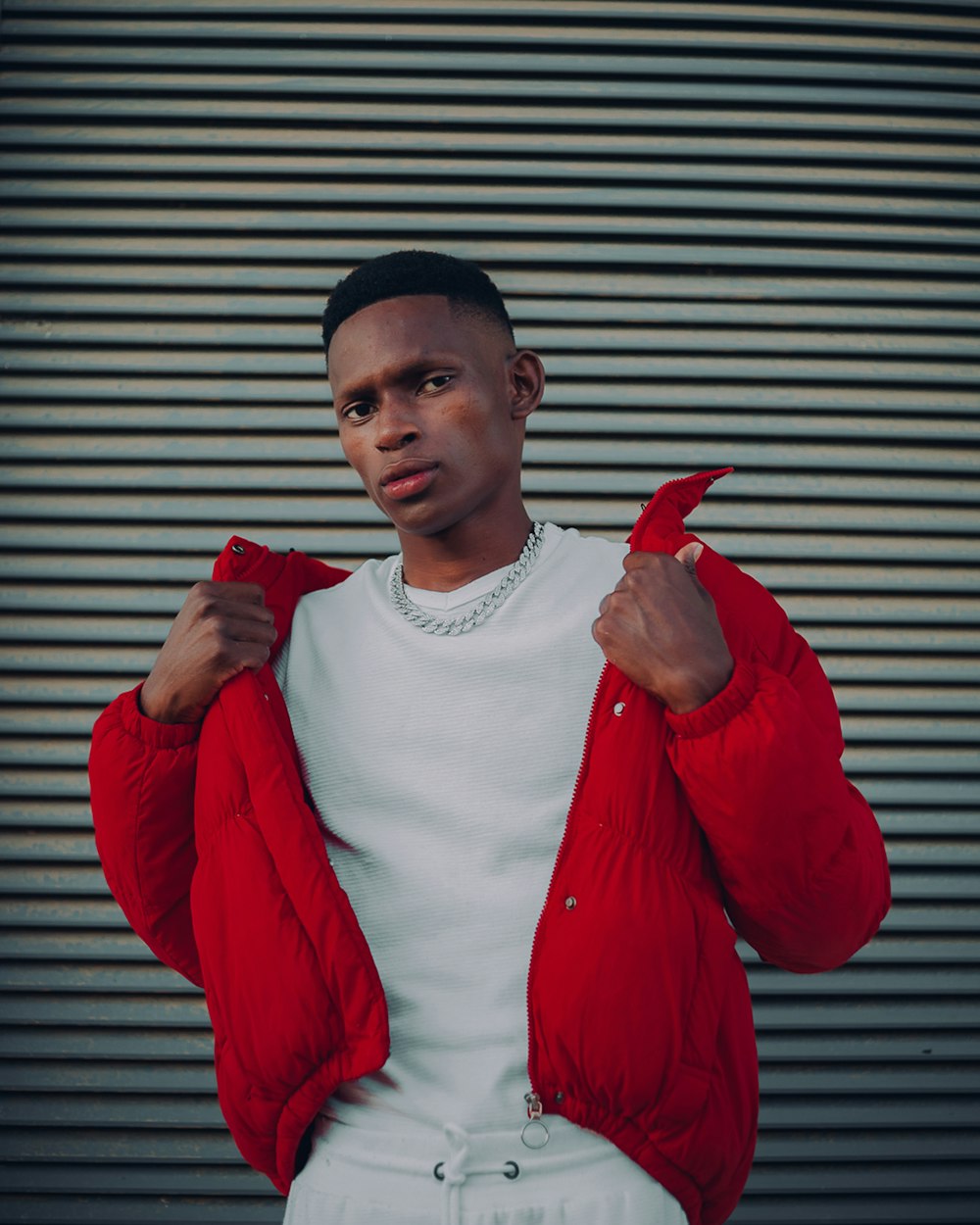 man in red jacket standing near window blinds