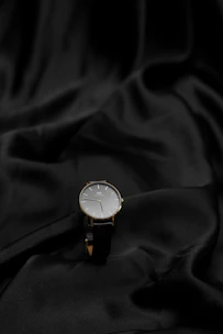 A sleek, minimalist wristwatch with a black leather strap displayed on a marble surface.