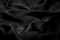 Smooth, dark, glossy fabric with soft folds and a silky texture, creating gentle shadows and highlights.