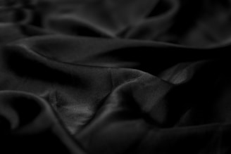 Smooth, dark, glossy fabric with soft folds and a silky texture, creating gentle shadows and highlights.