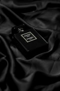 A black perfume bottle labeled Coco Noir by Chanel rests elegantly on a rich black silk fabric. The lustrous material provides a luxurious backdrop that accentuates the bottle's sleek and sophisticated design.