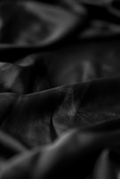 Soft, flowing fabric with numerous folds and creases in a rich, dark hue. The texture appears smooth and silky, with subtle light reflections enhancing its depth.