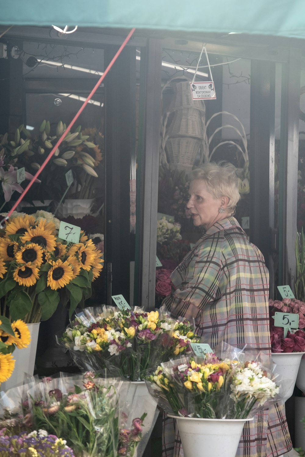 woman in brown and white plaid dress shirt standing beside flowers