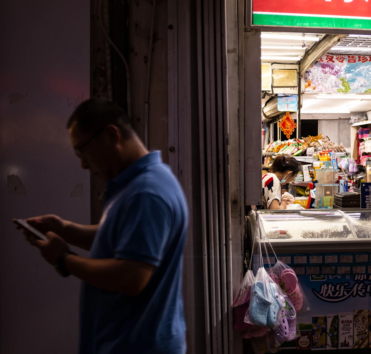 A small business owner standing in front of their shop, checking their phone with a slightly worried expression