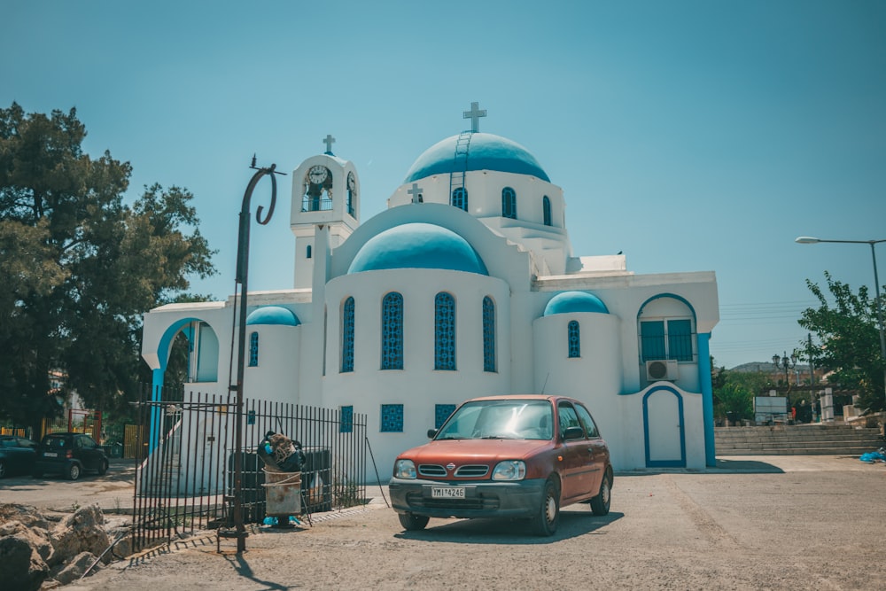 red sedan parked near white and blue concrete building during daytime