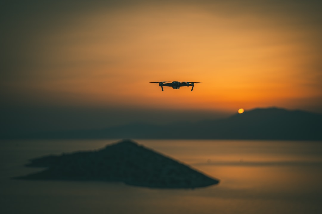 white and black drone flying over the sea during sunset