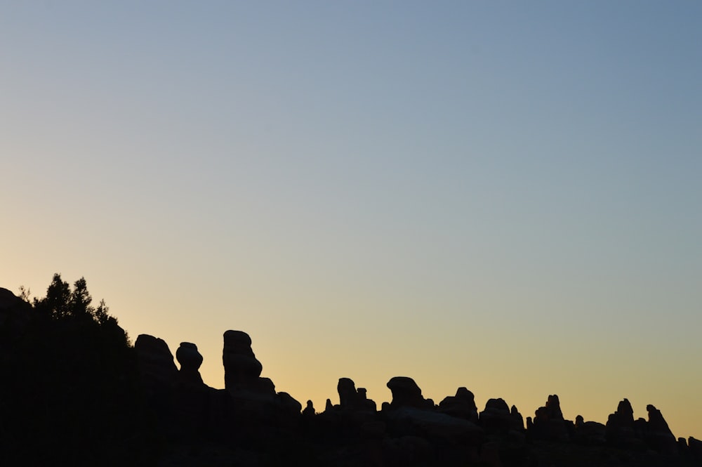 silhouette of people sitting on rock formation during sunset